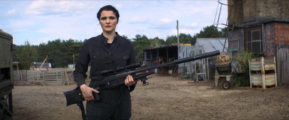 Melina walks across the property with her giant rifle.