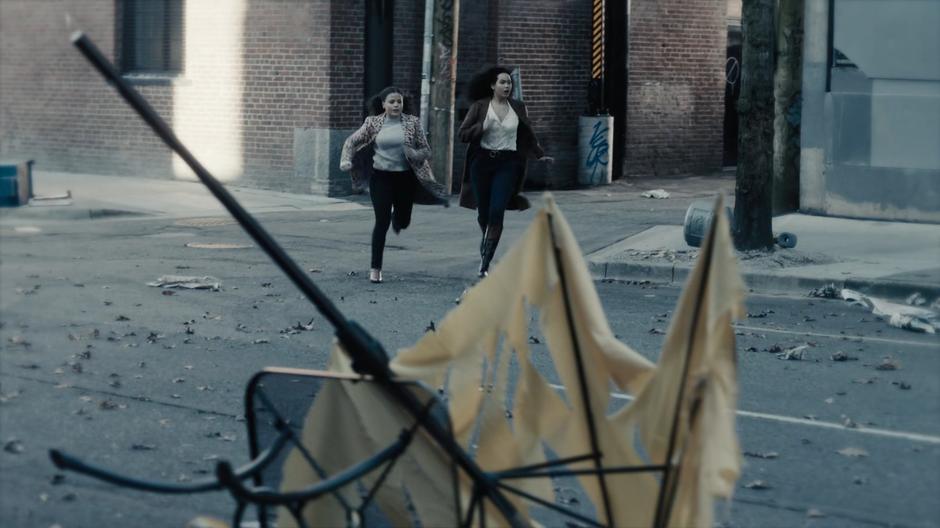 Maggie and Macy run out of an alley onto another deserted street.