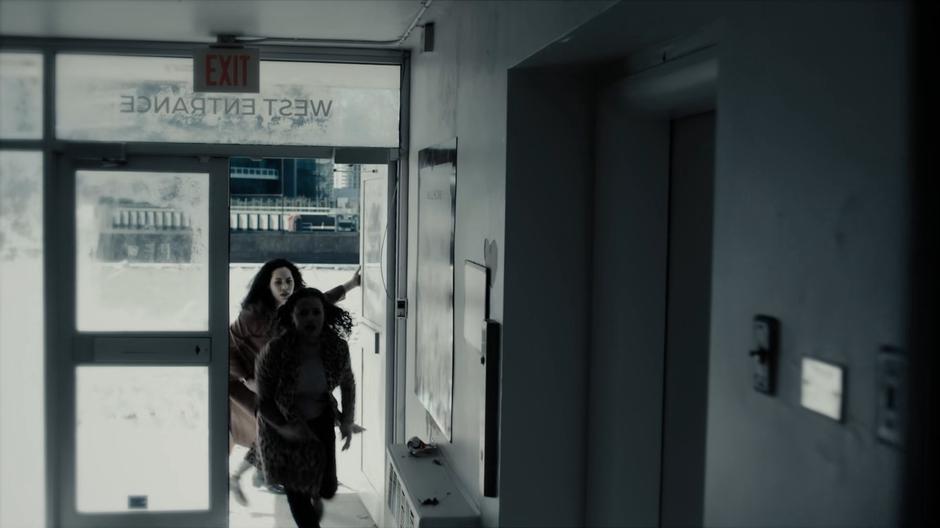 Maggie and Macy rush into the room containing the parking garage elevators.