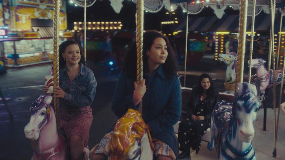 Maggie and Macy ride horses on the carousel while Mel sits behind them.