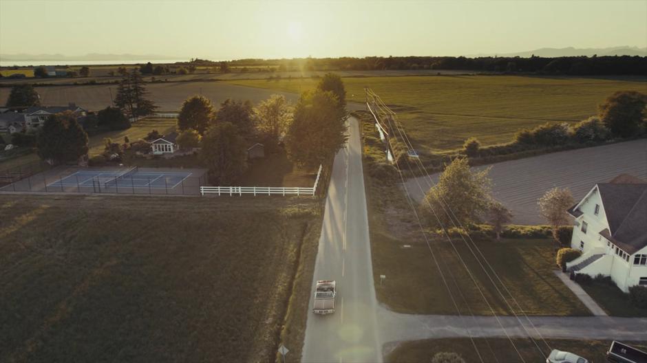 The Charmed Ones drive down a two-lane road leading through some farmland.