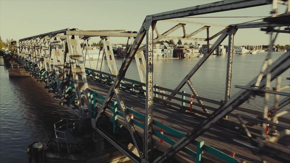 The car drives across a bridge near some houseboats.