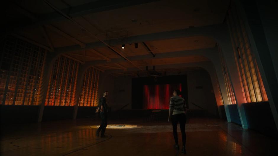 Macy approaches Jordan as he looks around the empty gym.