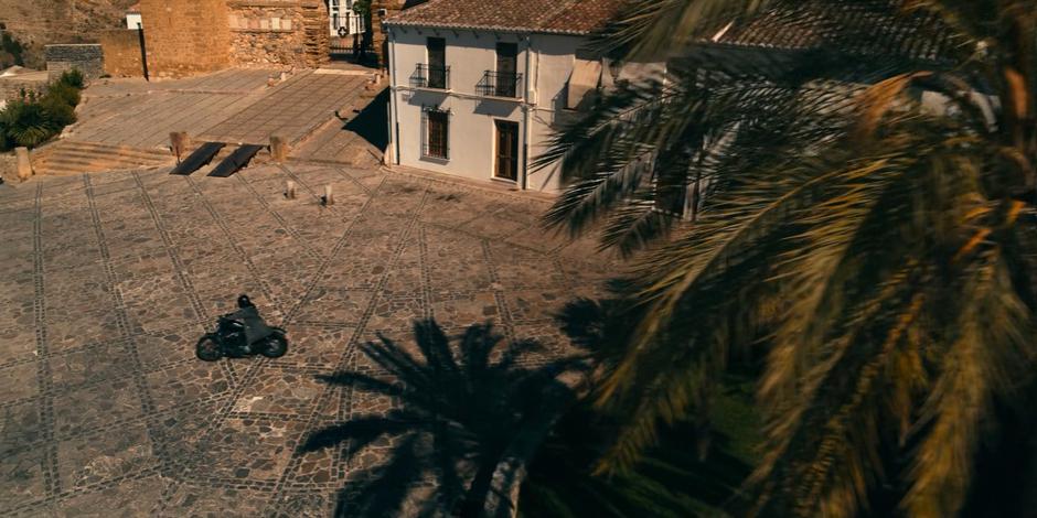 Mary rides her motorcycle through the plaza towards the gates of the Cradle.