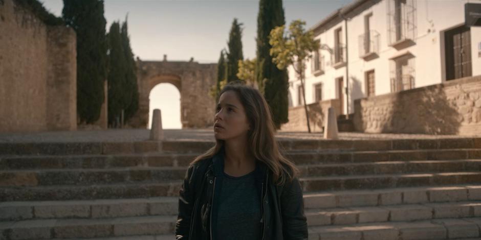 Ava looks around as she walks across the plaza to the building.