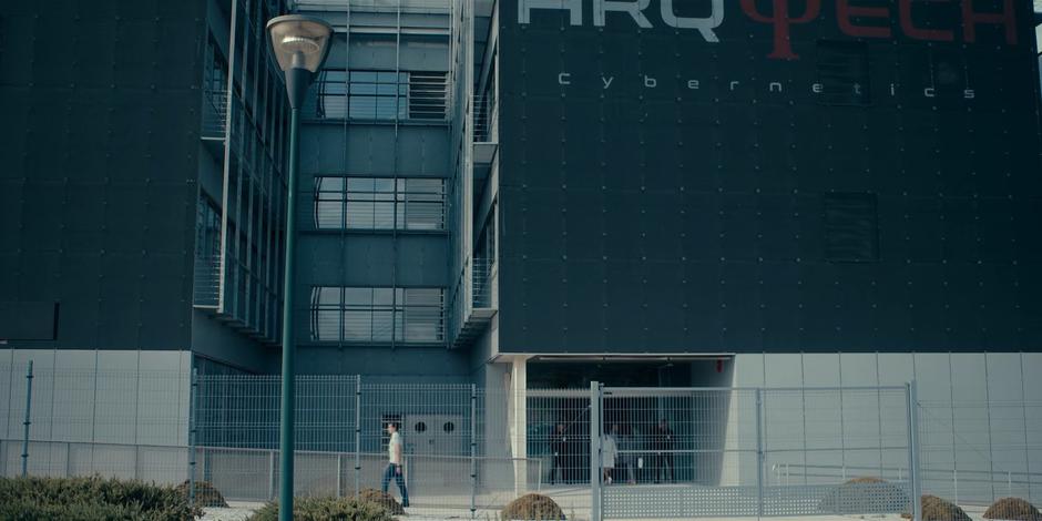 Ava enters the front entrance of the Arq Tech building.