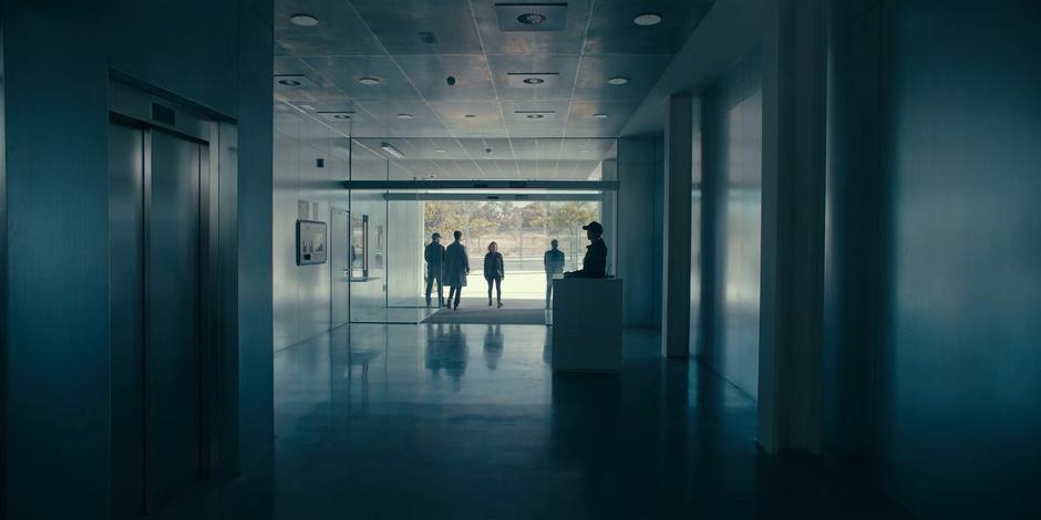 Ava walks into the Arq Tech lobby towards the receptionist's desk.