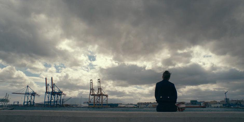 Ava sits on the concrete edge of the promenade looking out over the port.