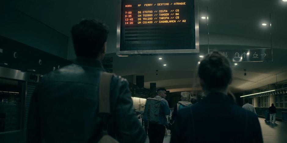 JC and Ava look up at the departure board in the ferry terminal.