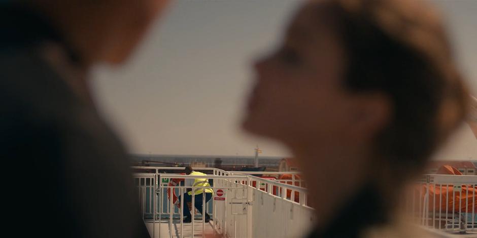 A ferry worker is visible in the distance between JC and Ava.