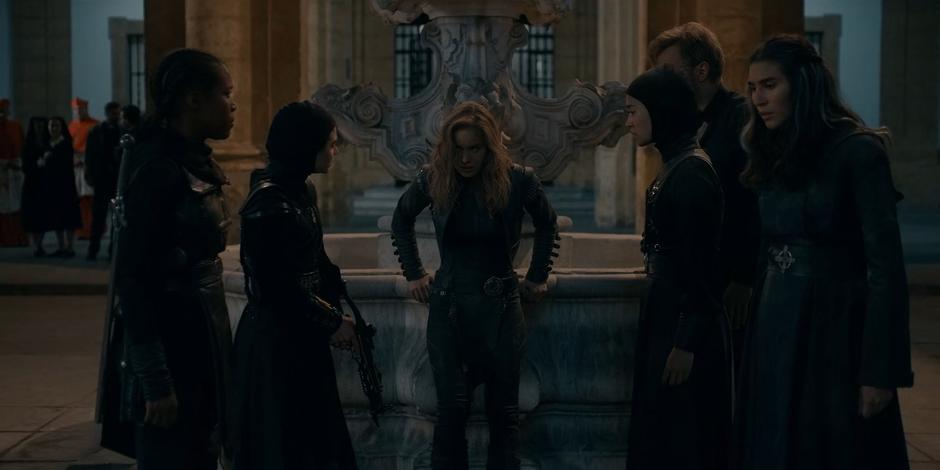 Ava leans against a fountain to recover her strength surrounded by Mary, Camila, Beatrice, Father Vincent, and Lilith.