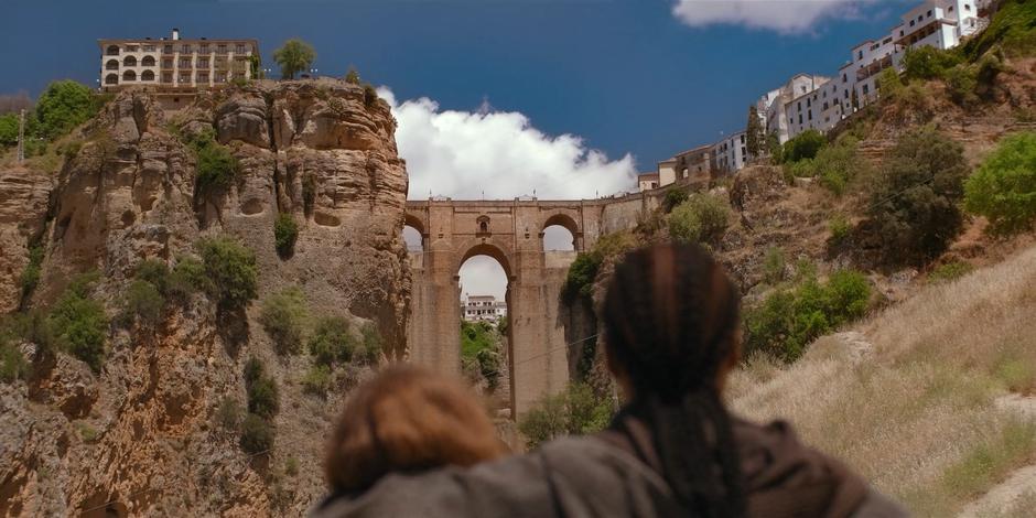 Ava stares up at the bridge high above while helping Mary stand.