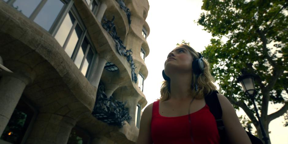 Henry admires the architecture as she wanders the street listening to music.