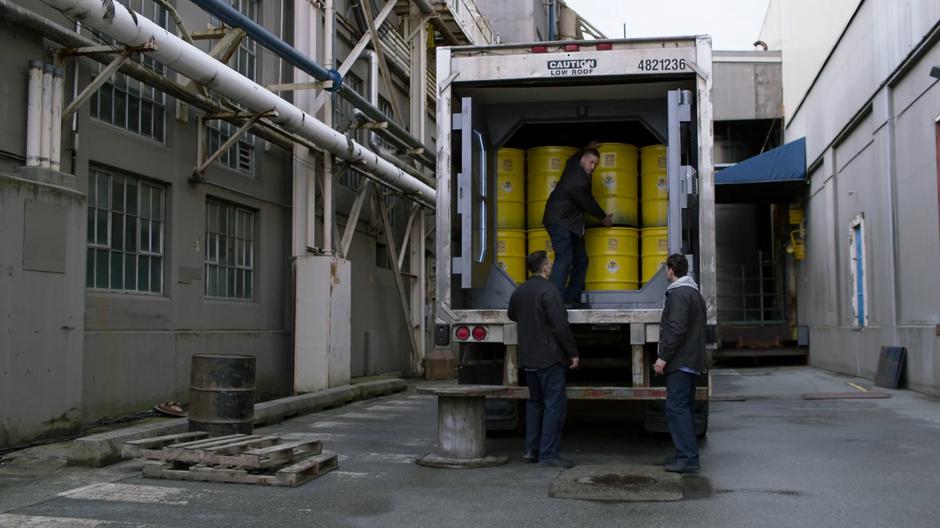 Three of the prisoners begin unloading the radioactive barrels from the back of the truck.