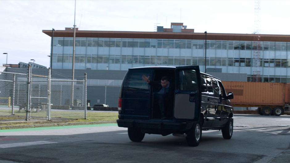 One of the alien prisoners leans out of the back of the van and uses his powers to cloak it from sight.