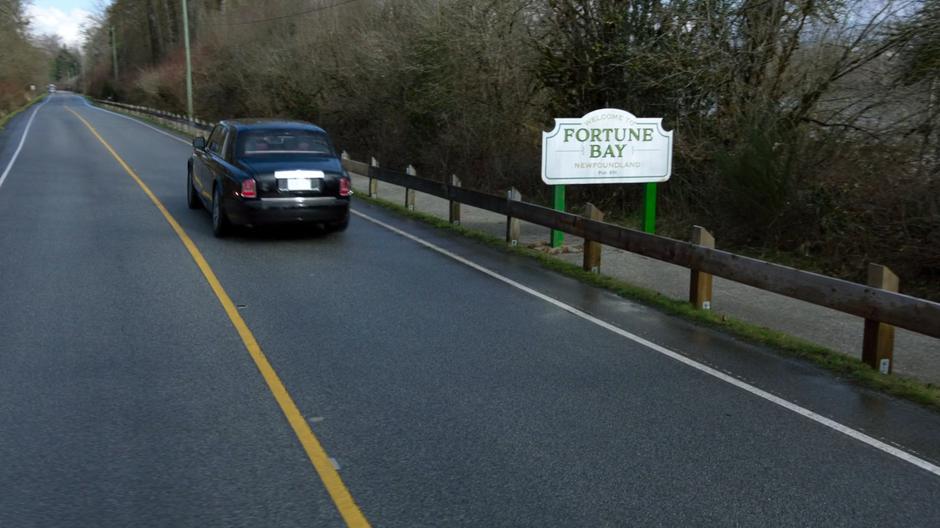 Lena's car drives past the Welcome to Fortune Bay sign.