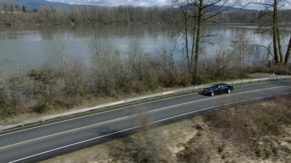 Lena's car drives down a winding road beside the water.