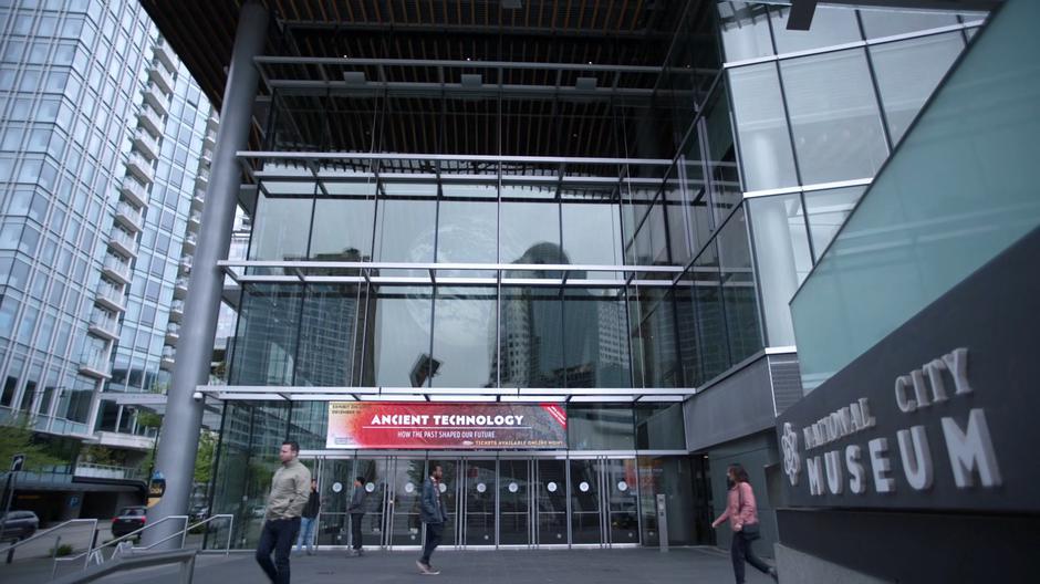 People walk past the front entrance of the museum with a banner advertising their Ancient Technology exhibit.