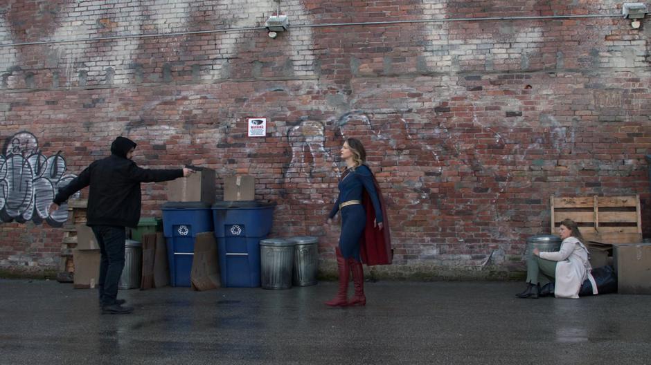 A man points his gun at Kara while she stands between him and a woman on the ground.