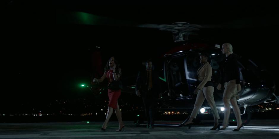 A woman in red exits her helicopter talking on the phone with several attendants following close behind.