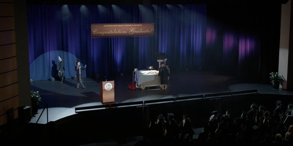 Liam Crandle comes out onto stage and approaches where Mary is standing in front of the gurney with Dr. Hall.