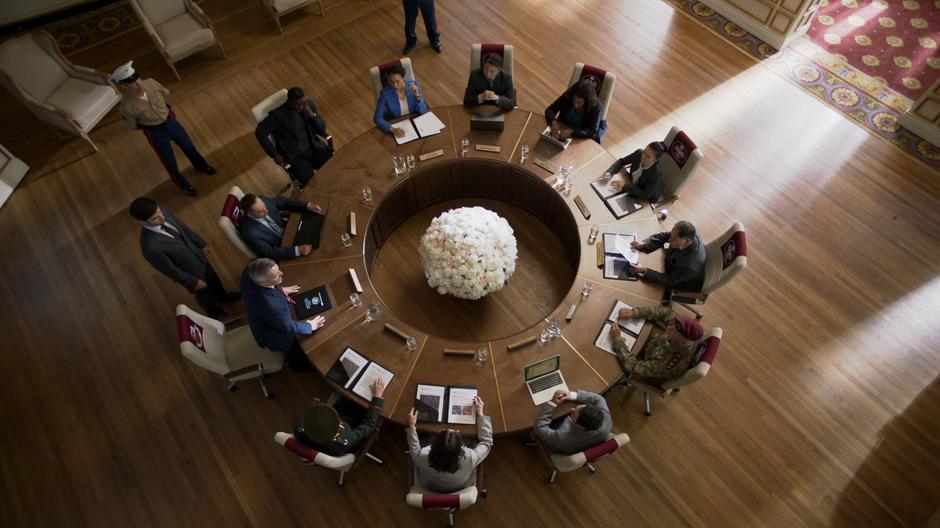 J'onn sits next to Secretary Brown as she mediates the peace talks.