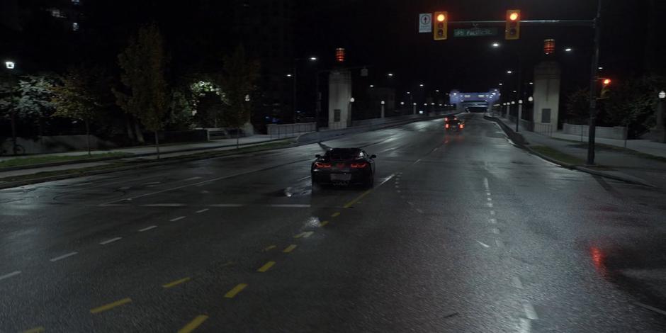 The Batmobile races through the intersection towards the bridge after the two vehicles.