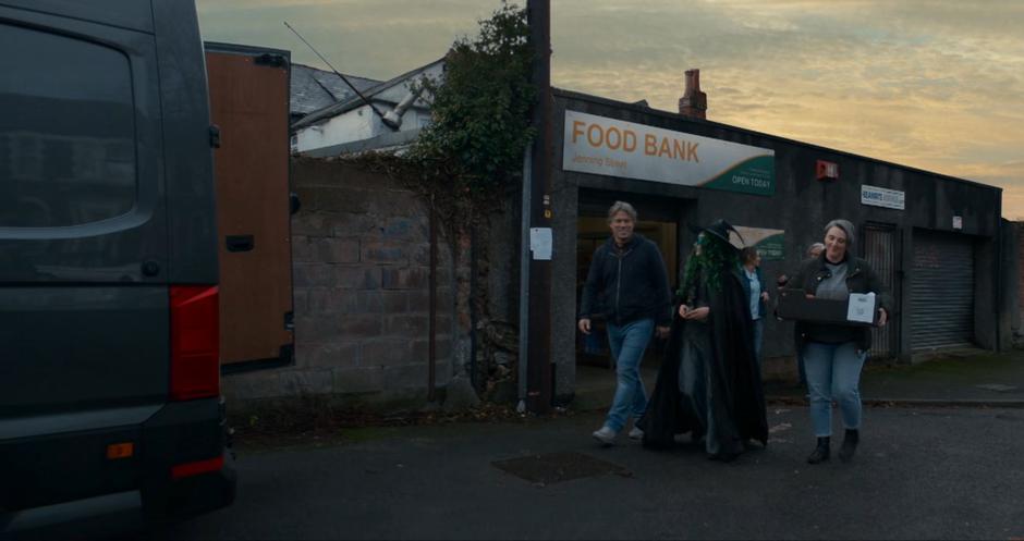 Dan walks with the kid an a woman with a box of food over to a van.