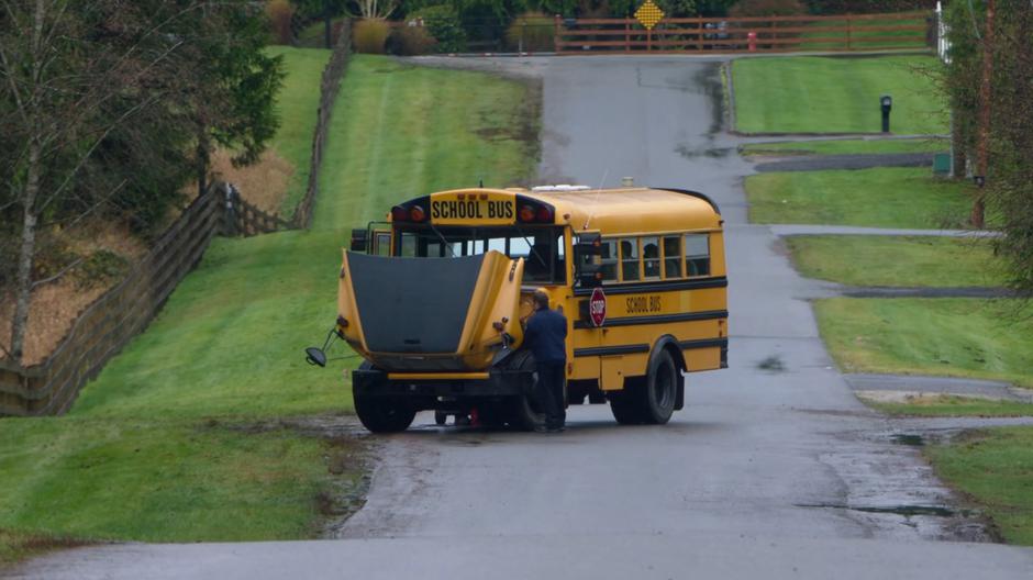 A school bus driver works on the engine of his bus which is stalled in the middle of the road.