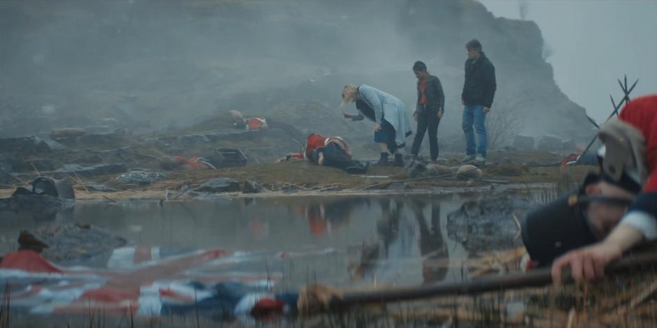 Yaz and Dan watch as the Doctor leans down to examine one of the bodies of a soldier.