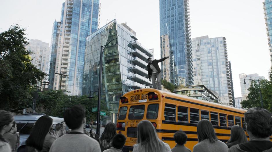 Orland stands atop a school bus and gives a speech to all of the grey people in the street.