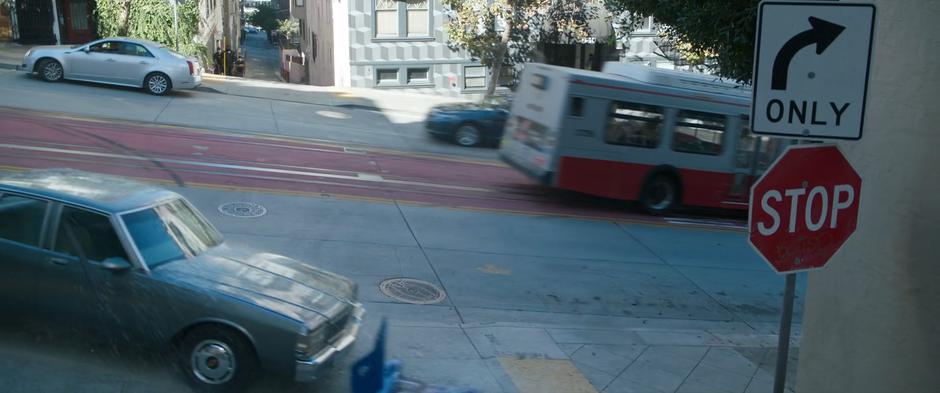 The bus speeds down the hill as the car it hits swerves up onto the sidewalk.