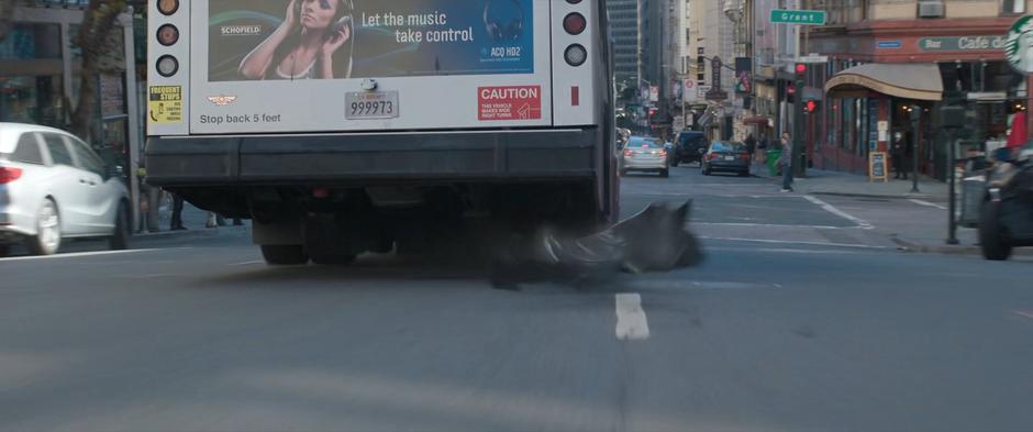 A piece falls off the bus as it drives through an intersection.