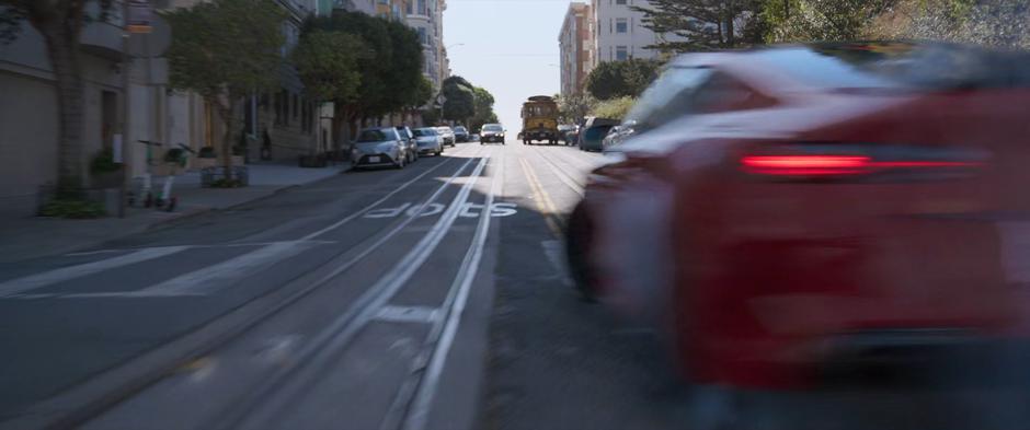 Katy swerves the red car around the corner and up a hill towards a streetcar.