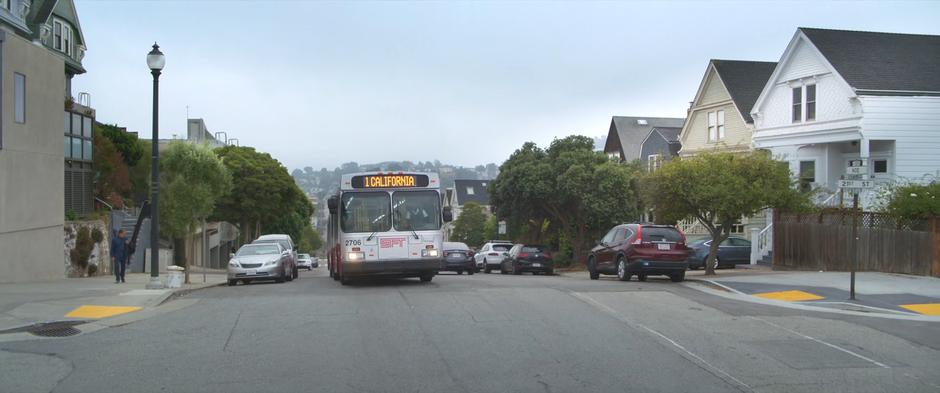 The "1 California" bus drives up over a hill on its route.