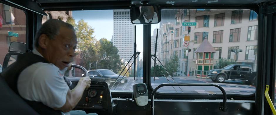 The bus driver looks over his shoulder as the bus drives through an intersection towards a car turning left in front of it.