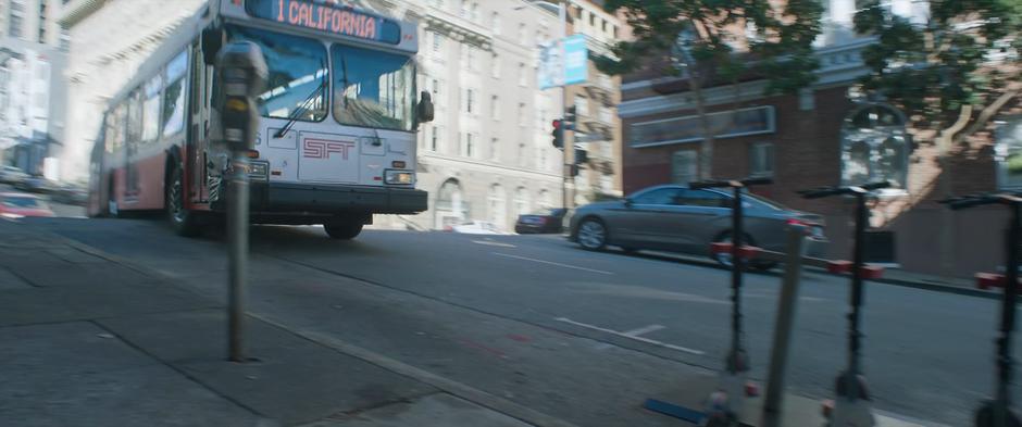 The bus turns towards the side of the road where some scooters are parked.