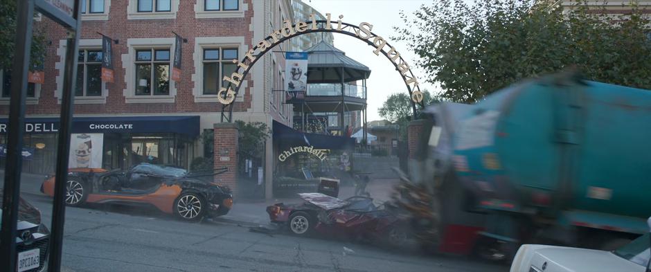 Crushed cars are left in the wake of the bus as is speeds down the hill past a Ghiradelli Square sign.