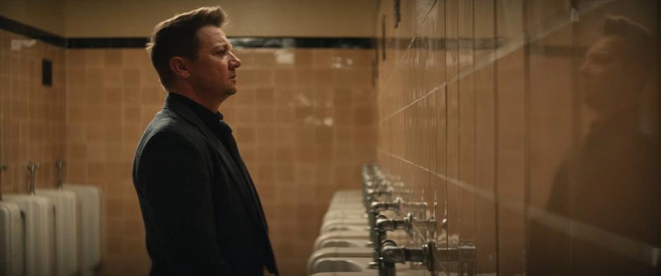 Clint stands at a urinal in the bathroom.