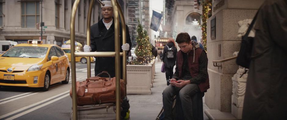 Cooper watches the video of Kate from the night before on his phone while waiting on the sidewalk outside the hotel.