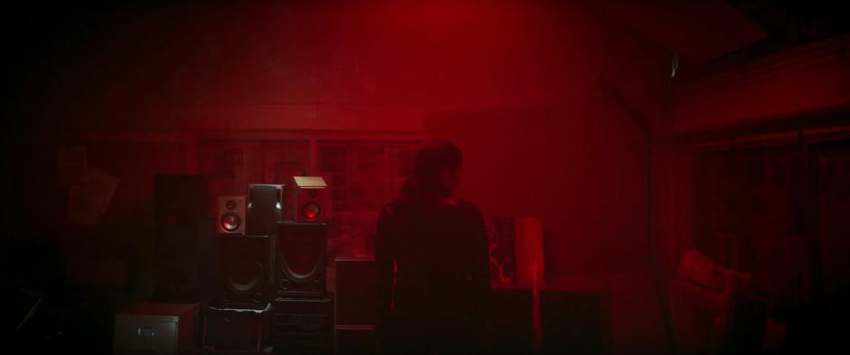 The woman in charge of the Tracksuit Mafia stands in a room bathed in red light in front of a stack of speakers.