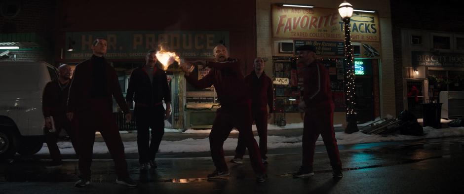 Several members of the Tracksuit Mafia stand on the street while one prepares to throw another Moltov cocktail through Kate's window.