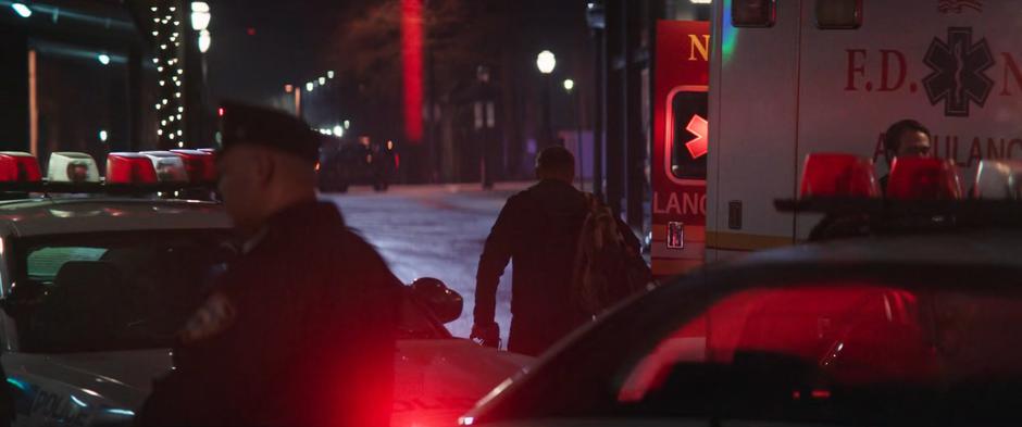 Clint walks off down the street past an ambulance after searching the apartment.