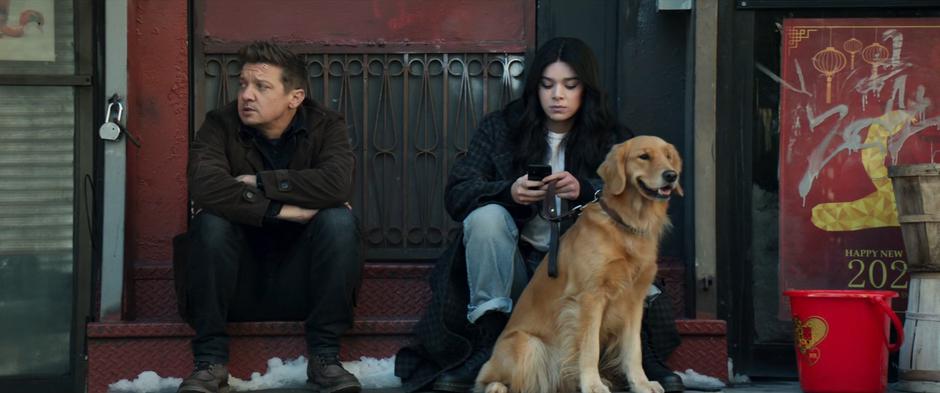 Clint glances around while Kate texts him and holds Pizza Dog's leash.
