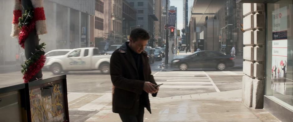 Clint calls his wife on the phone while walking down the street.