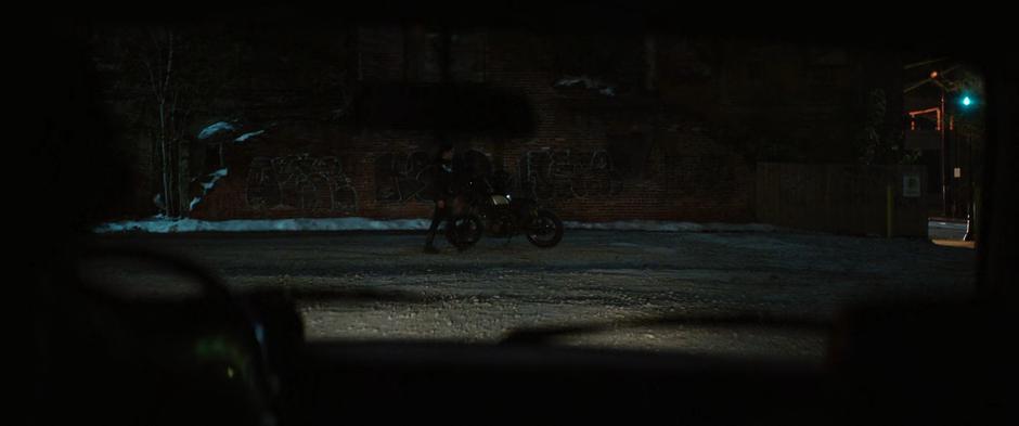 Maya is visible standing in the lot next to her motorcycle through Kazi's windshield.