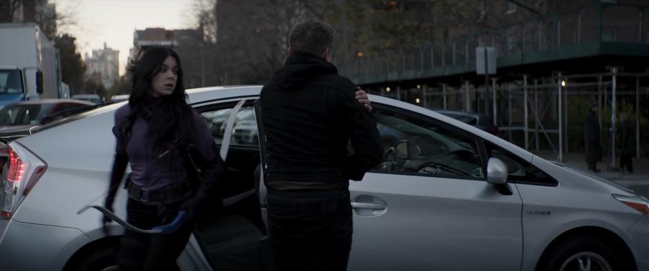 Clint holds the door of the rideshare open for Kate as he massages his injured shoulder.