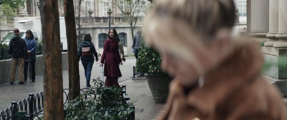 Eleanor checks around the sidewalk before entering the building while Yelena ducks her head.