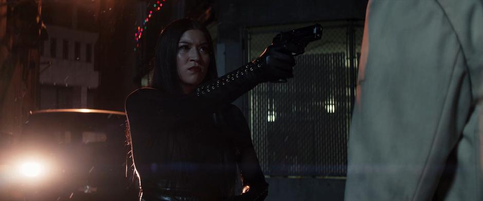 Maya points her gun at Fisk while being backlit by the headlights of the van.