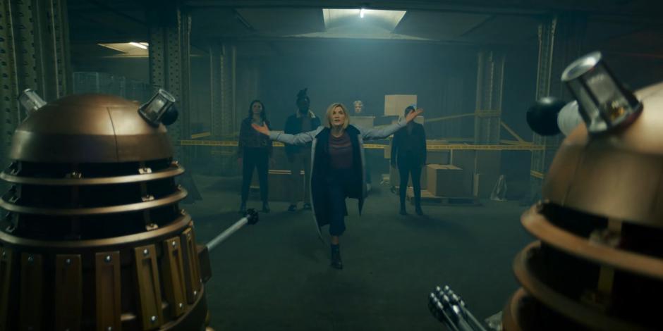 The Doctor stands in front of Sarah, Nick, Dan, and Yaz and taunts the Daleks.